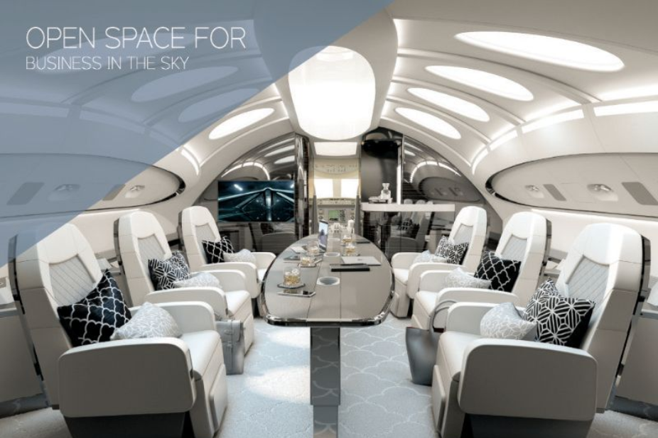 Luxury business jet interior with white seating, a long table, and a large monitor.