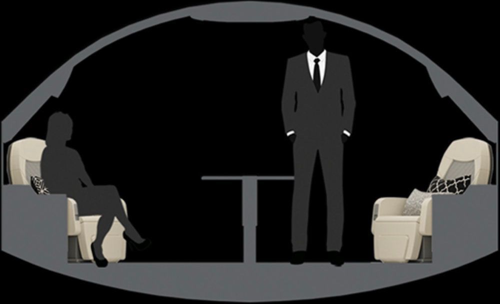 Interior of a private jet cabin: a man and woman sit, and stand near a table.