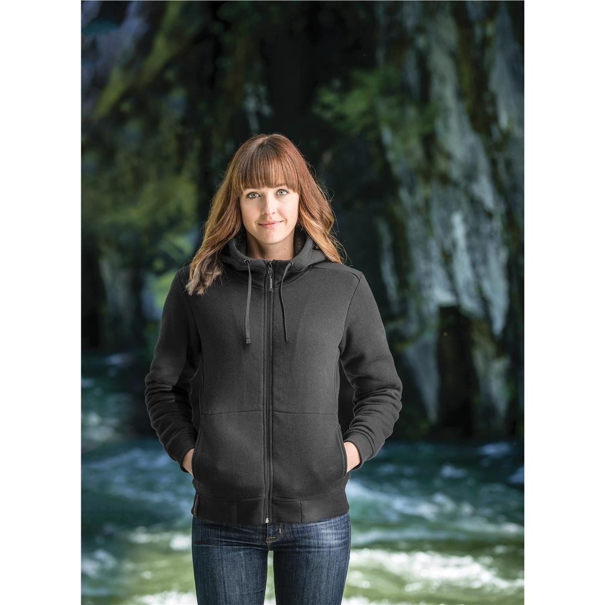 A woman wearing a black hoodie is standing in front of a river.