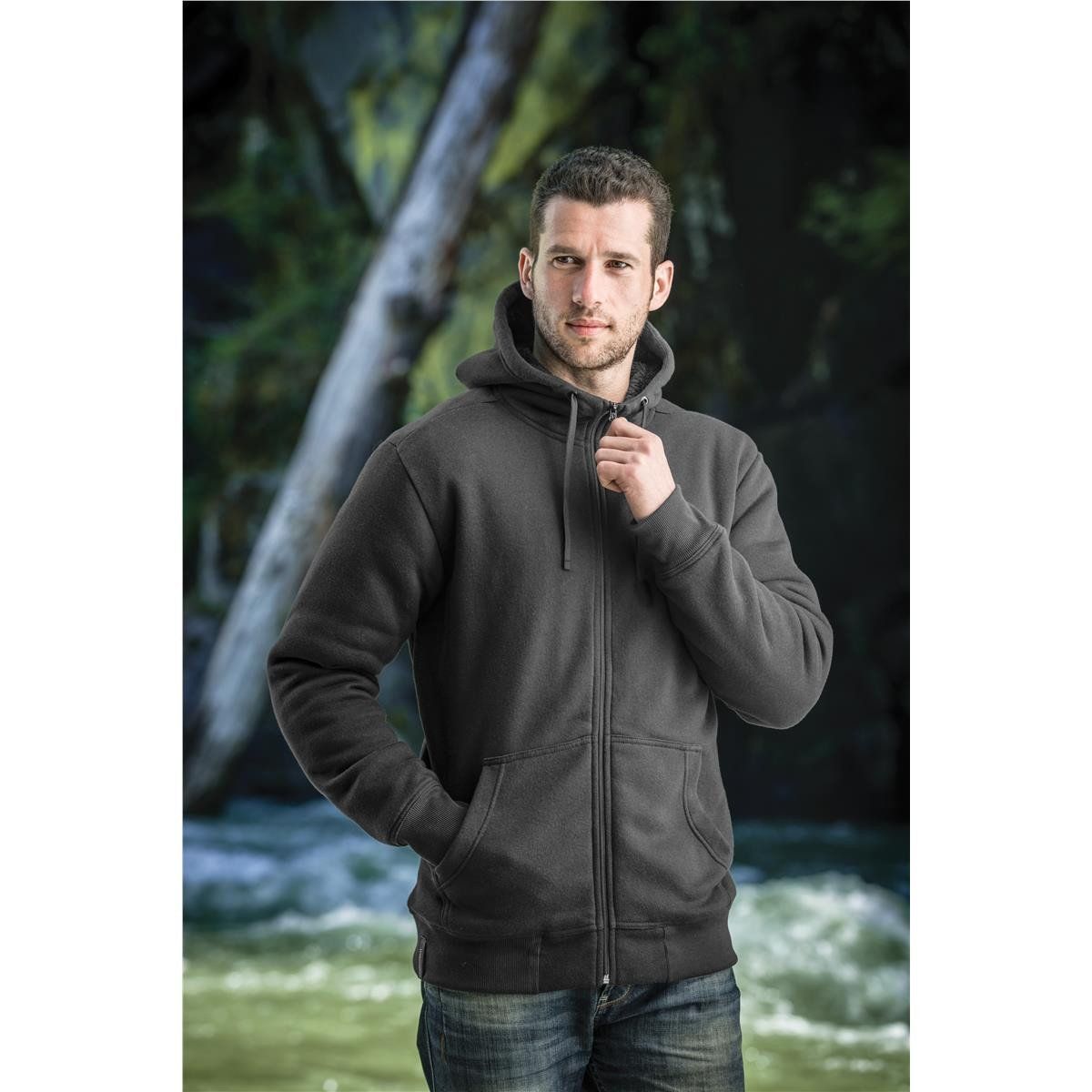 A man wearing a black hoodie is standing in front of a river.
