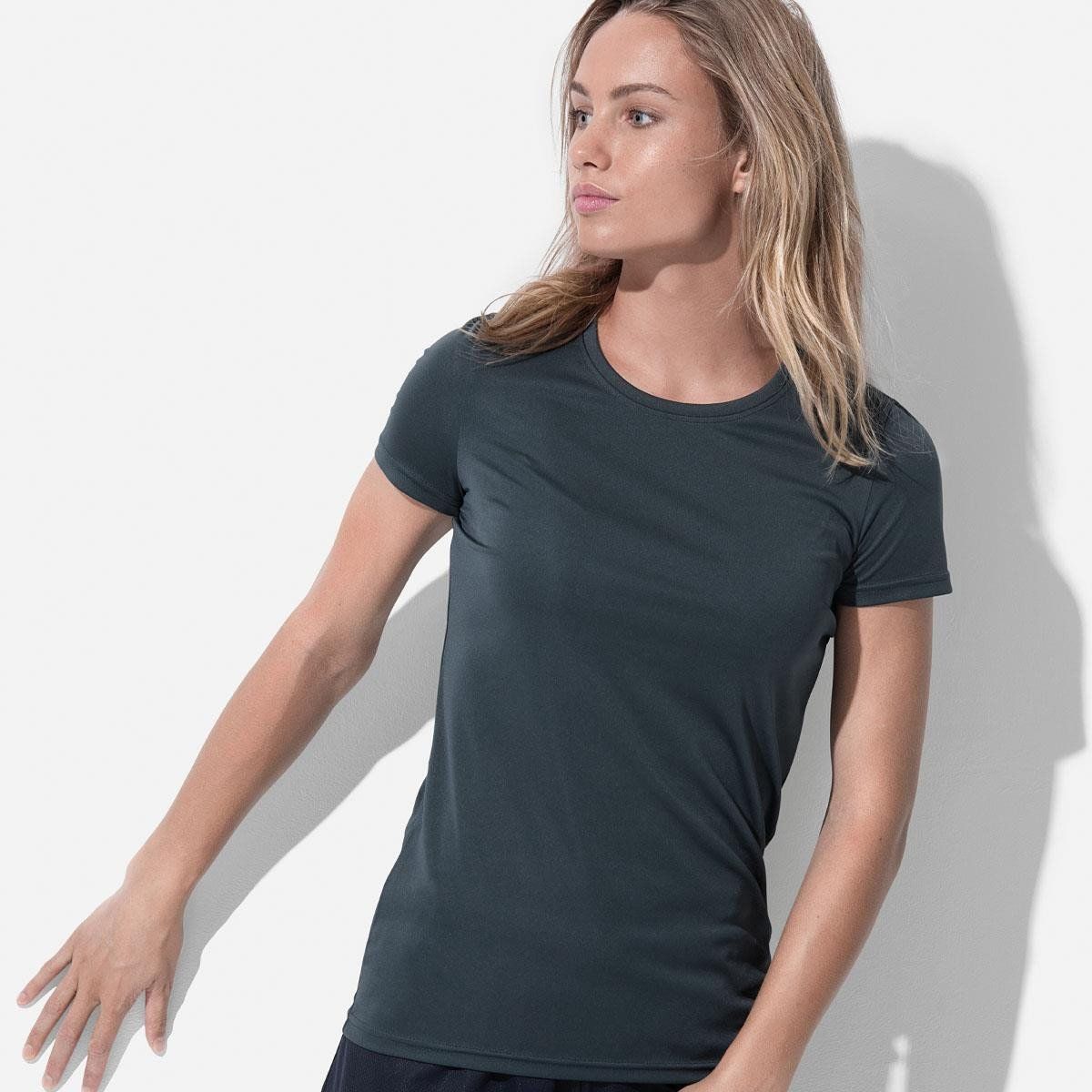 A woman wearing a black t-shirt is leaning against a white wall