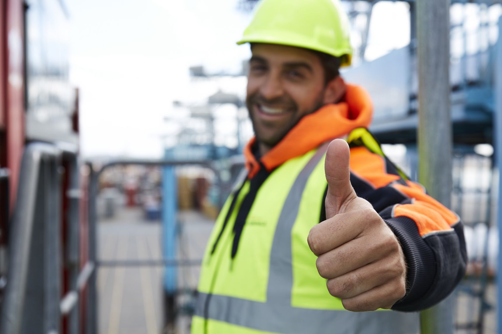 A man wearing a hard hat and safety vest is giving a thumbs up.