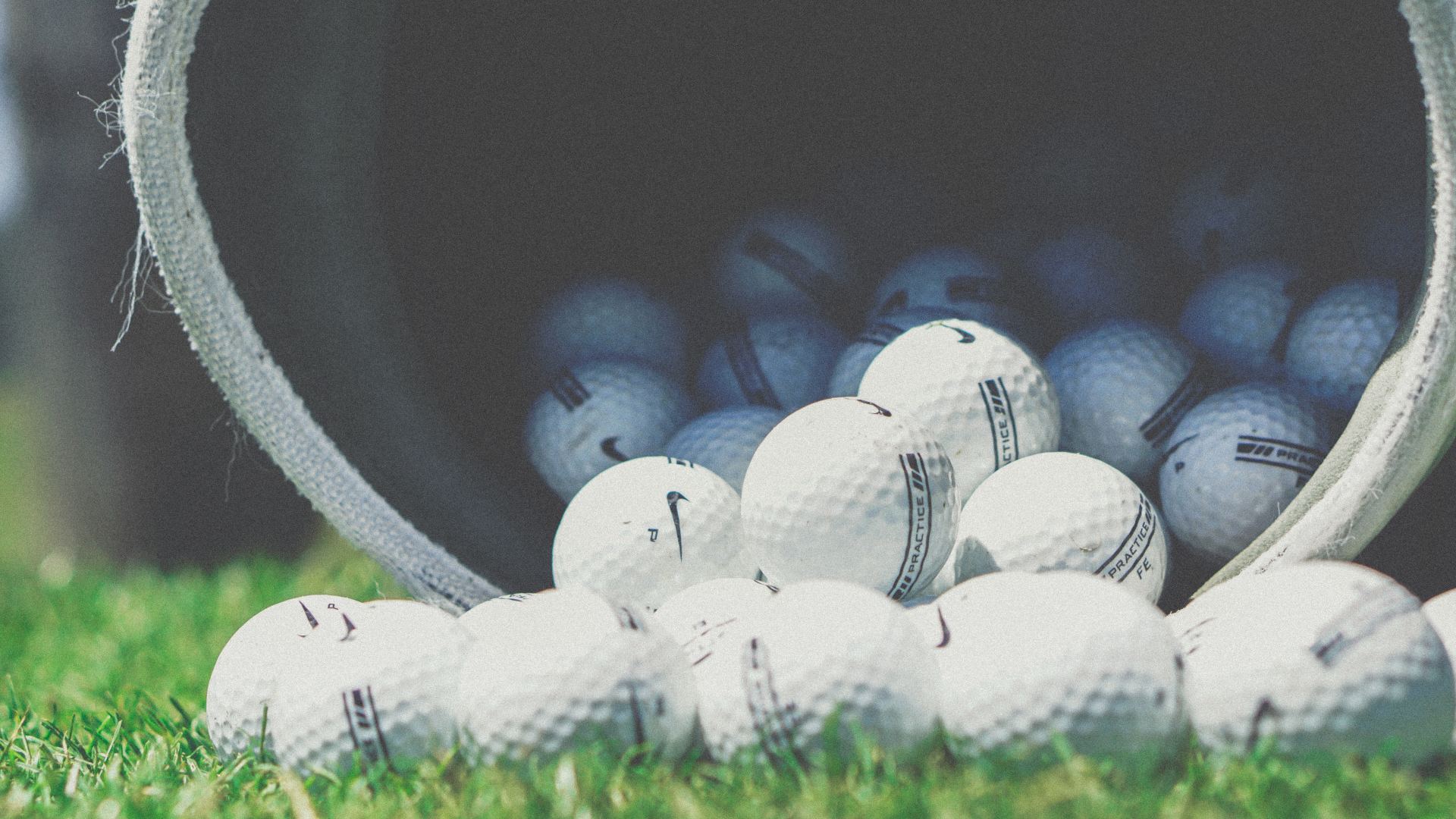 A bucket filled with golf balls is sitting on top of a lush green field.