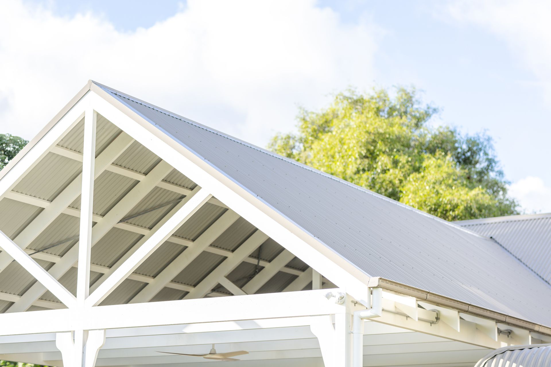 White-framed pergola with gray corrugated metal roof, against a bright sky and trees — Stark Building & Constructions In Nowra, NSW