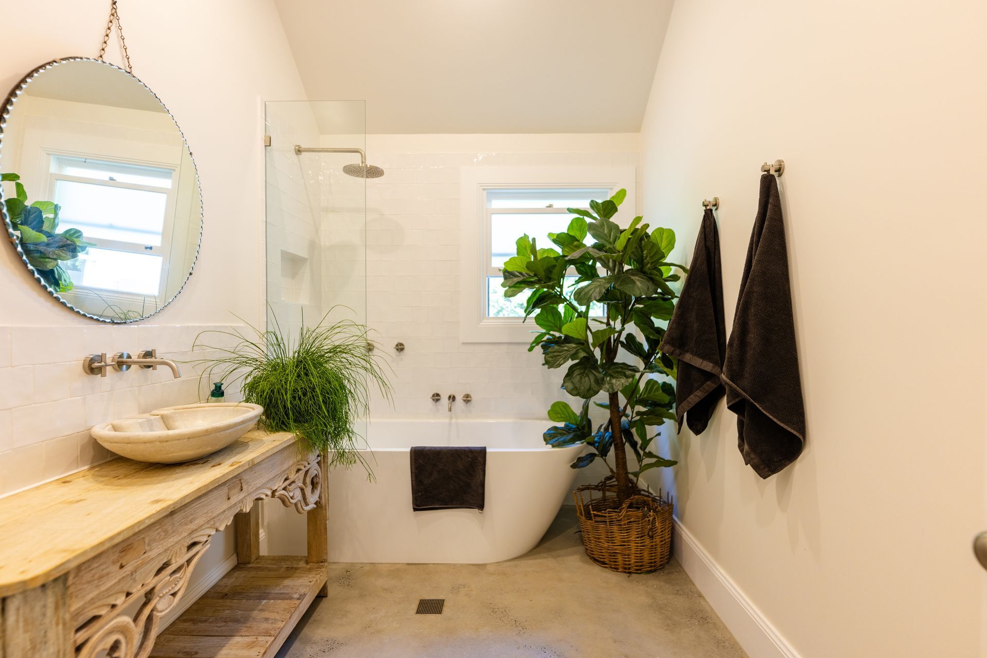 Bathroom with a round mirror, wooden vanity, freestanding tub, and a large potted plant  — Stark Building & Constructions In Berry, NSW