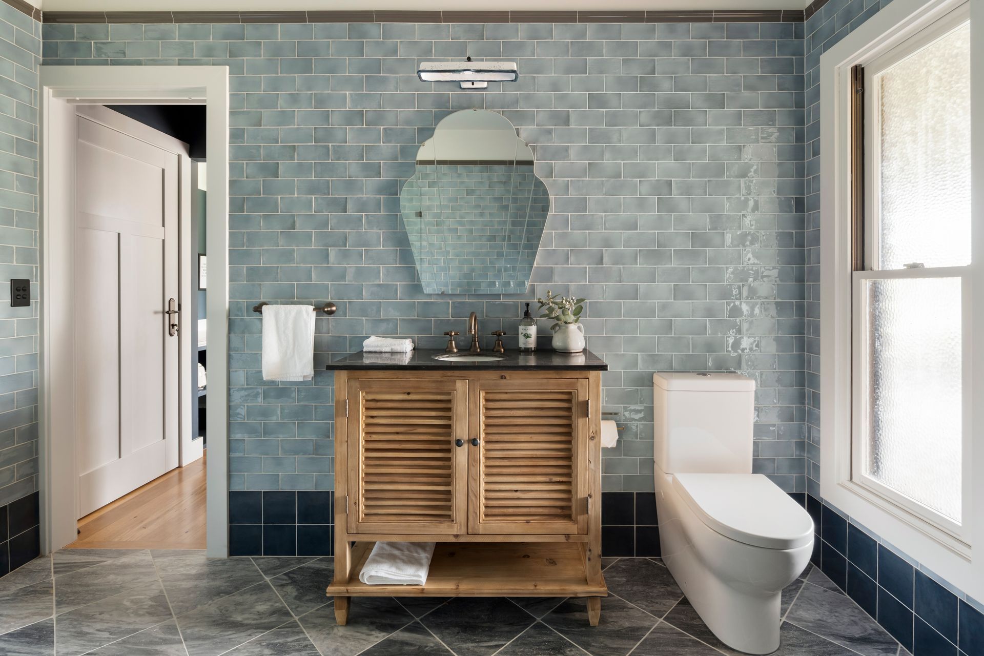 Bathroom with blue tile walls, wooden vanity, white toilet, and an open doorway  — Stark Building & Constructions In Nowra, NSW