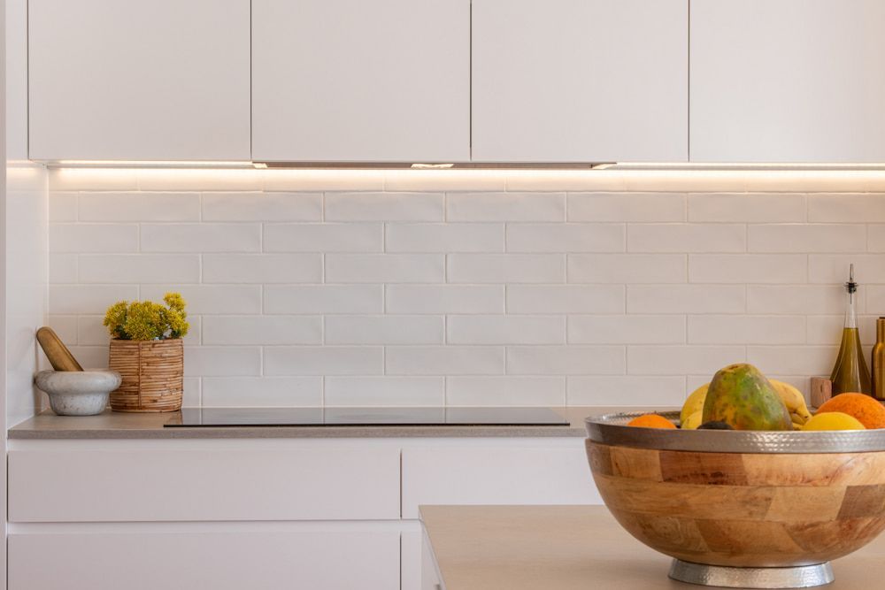 White kitchen with fruit bowl, flowers, and white tile backsplash — Stark Building & Constructions In Shoalhaven, NSW