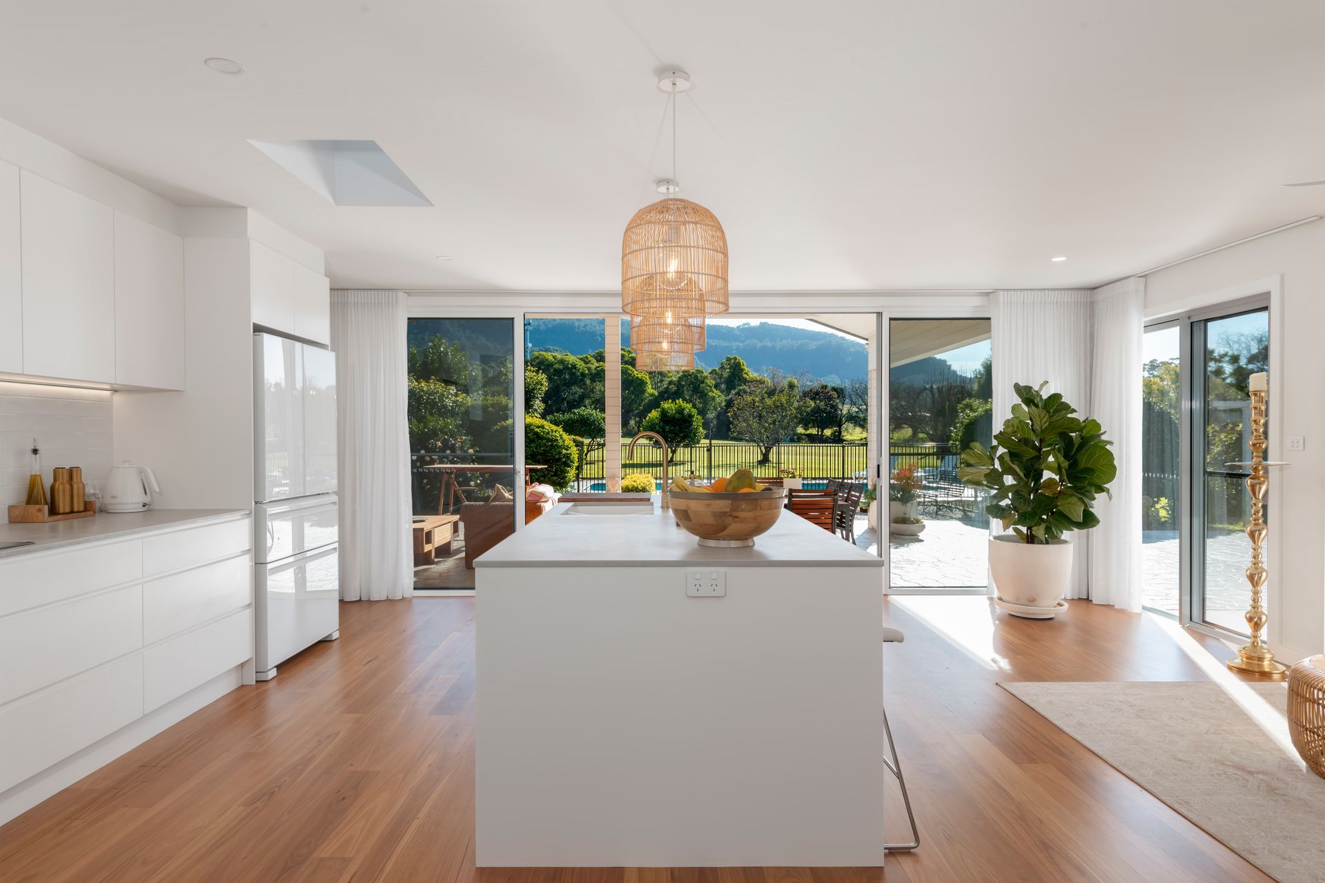 Bright, modern kitchen with white cabinets, island, and large glass doors opening to a green outdoor view — Stark Building & Constructions In Nowra, NSW
