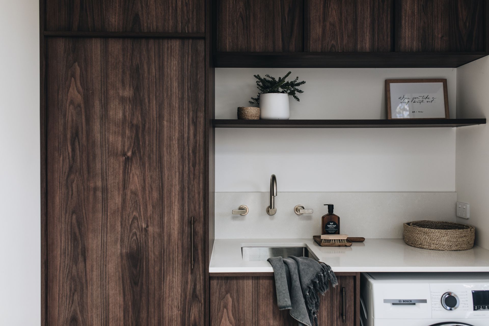 Laundry room with dark wood cabinets, white countertop, sink, and shelves with decor  — Stark Building & Constructions In Kiama, NSW