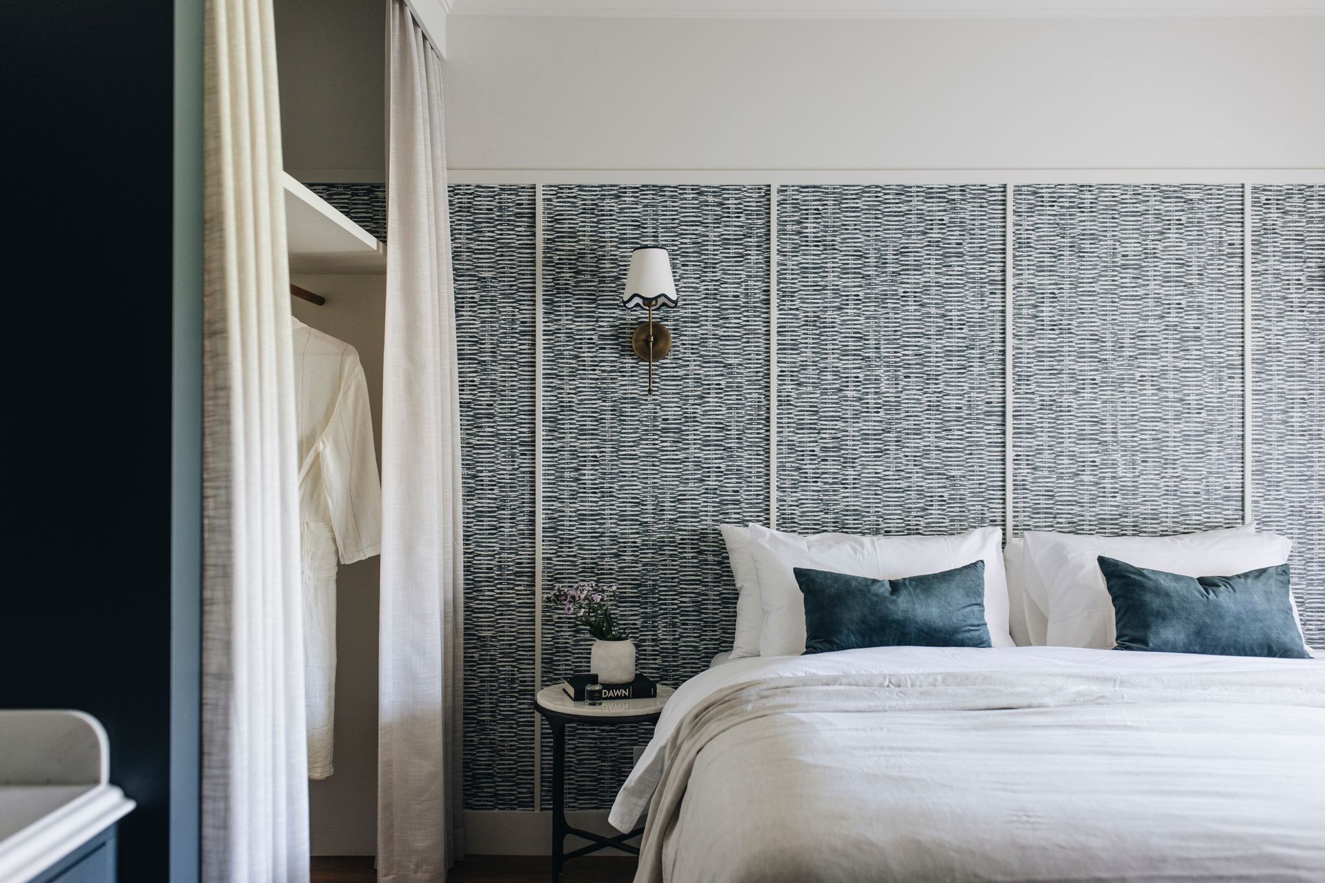 Bedroom with white bedding, blue pillows, patterned wall, and a robe in the closet  — Stark Building & Constructions In Nowra, NSW