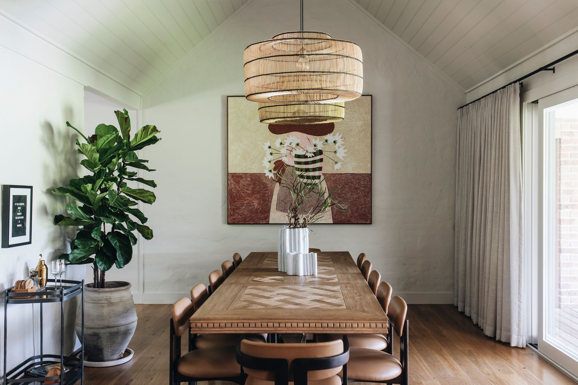Dining room with long wooden table, chairs, art, chandelier, and potted plants  — Stark Building & Constructions In Berry, NSW