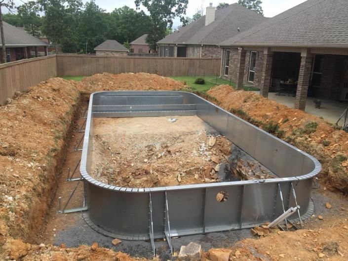 A rectangular metal swimming pool frame sits inside an excavated dirt hole in a suburban backyard.