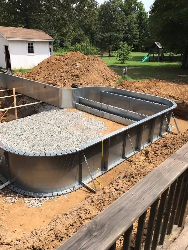 A metal swimming pool frame under construction in a dirt backyard with a shed in the background.