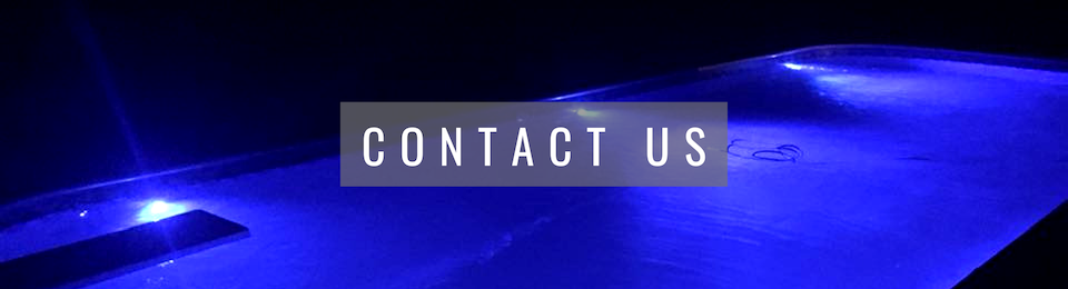 A swimming pool at night illuminated with bright blue underwater lights, featuring a 