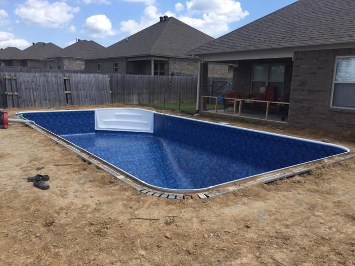 An in-ground swimming pool with a blue patterned liner and white steps in a backyard under construction.