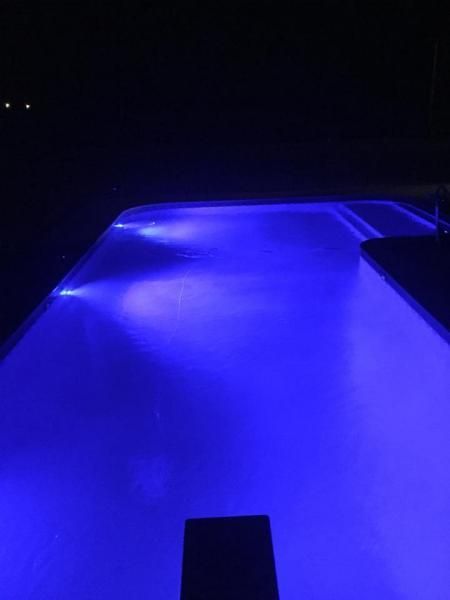 A rectangular swimming pool at night, illuminated by bright blue underwater lights.