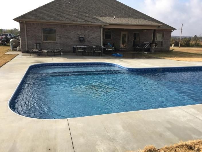 A backyard swimming pool with blue water and a concrete deck beside a brick house.
