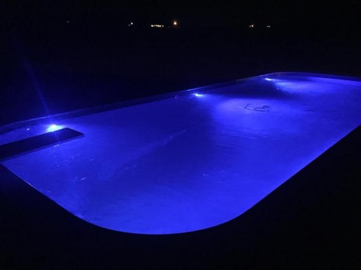 A swimming pool at night illuminated with vibrant blue underwater lights.