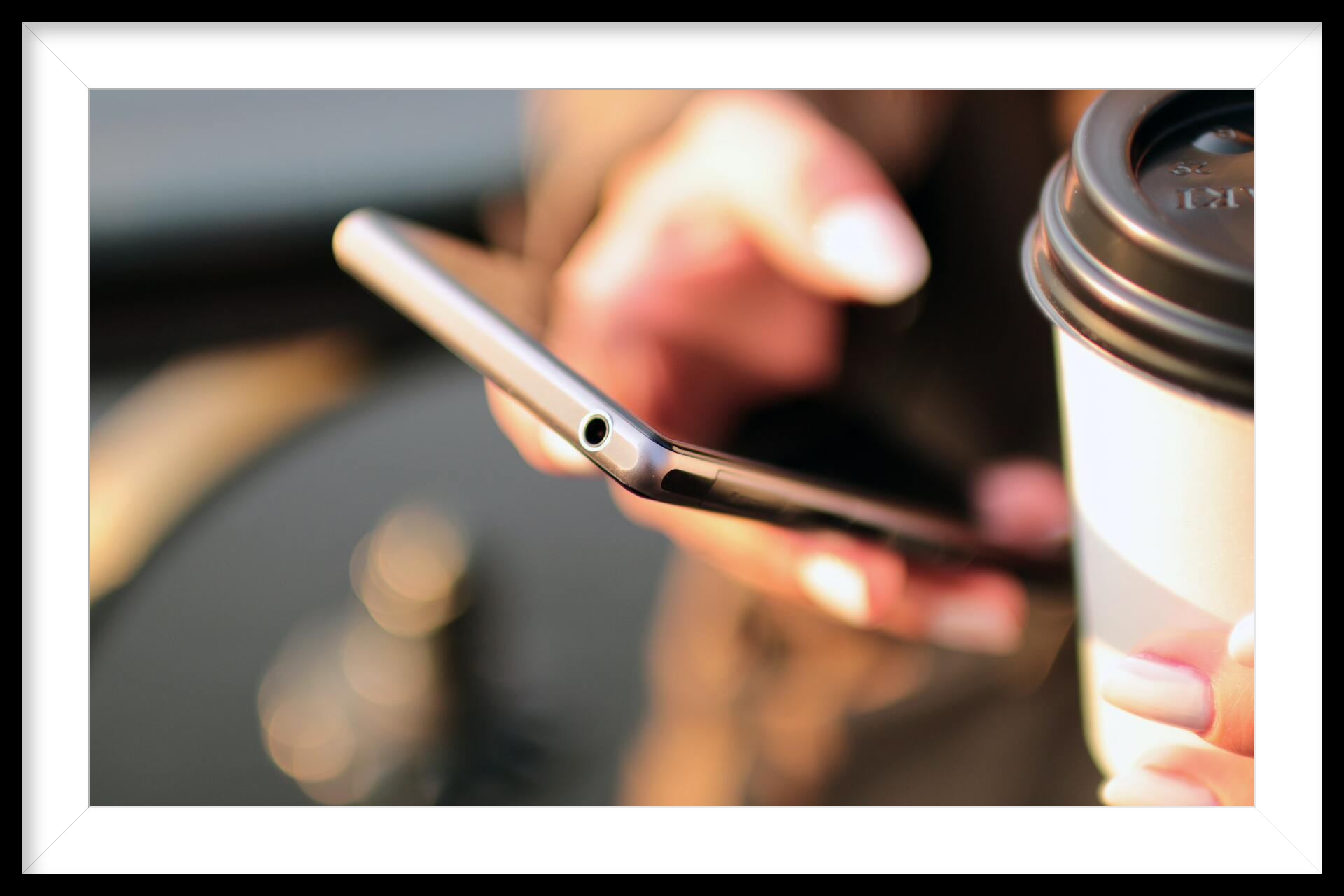 a person is holding a cup of coffee and using a cell phone