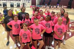 Group of cheerleaders in bright pink shirts posing together in a gym