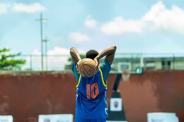 Athlete in blue jersey with orange number 10 stands with hands behind head on an outdoor court