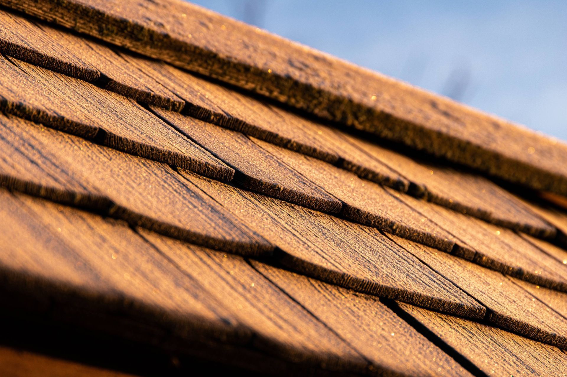 A close up of a wooden roof with shingles against a blue sky.