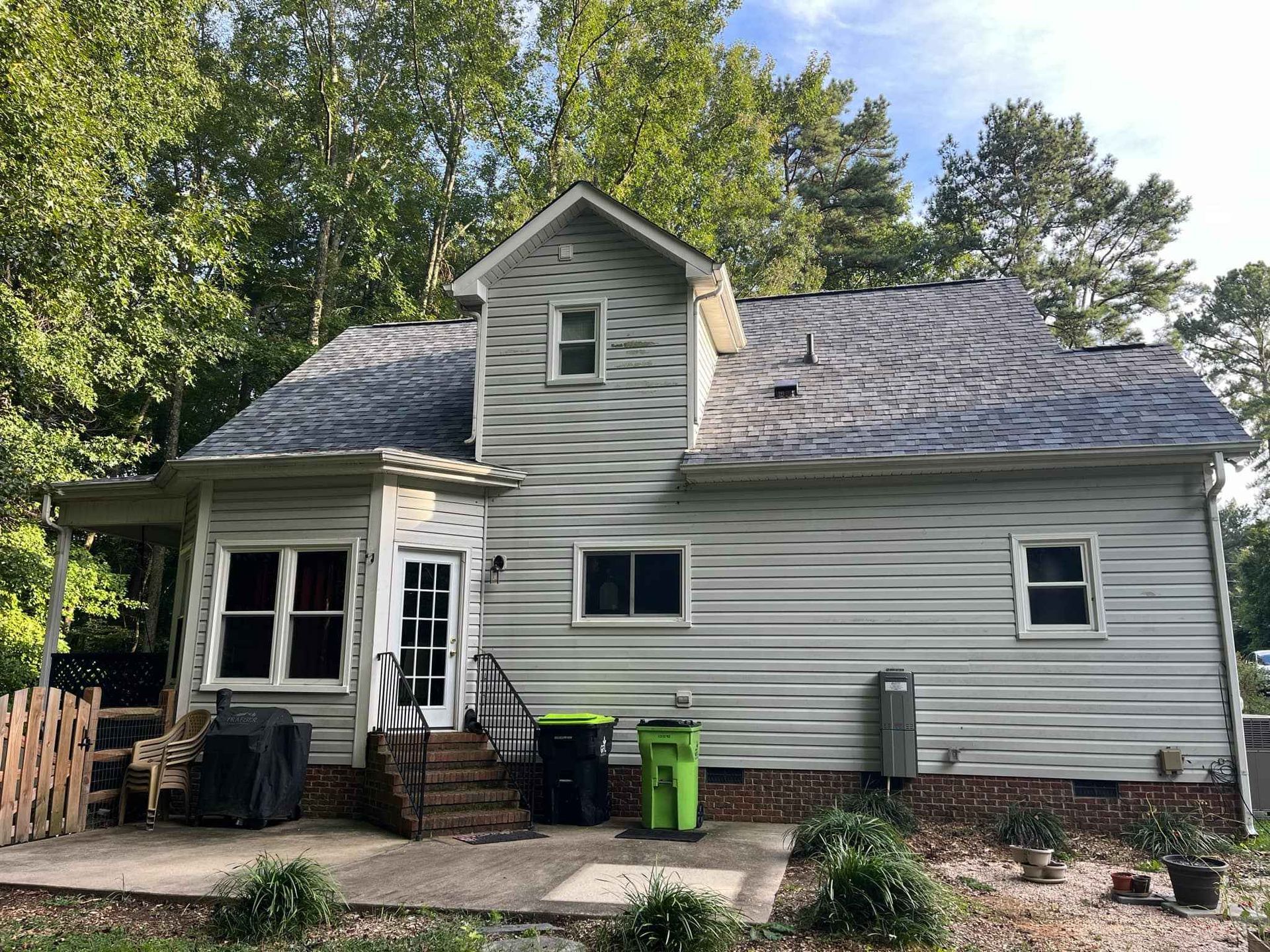 A white house with a gray roof and green trash cans in front of it.
