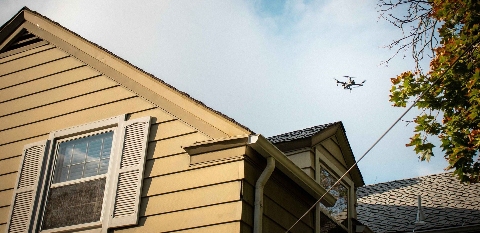 A drone is flying over a house with a tree in the foreground.