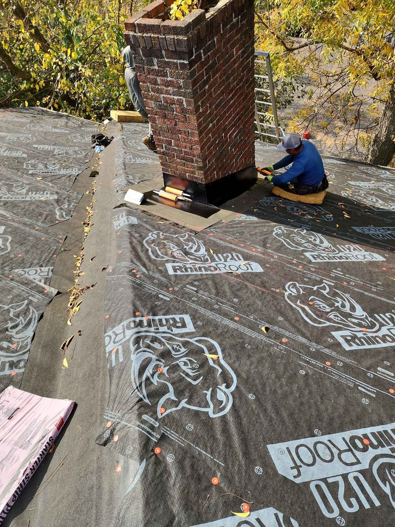 A man is sitting on a roof working on a chimney.