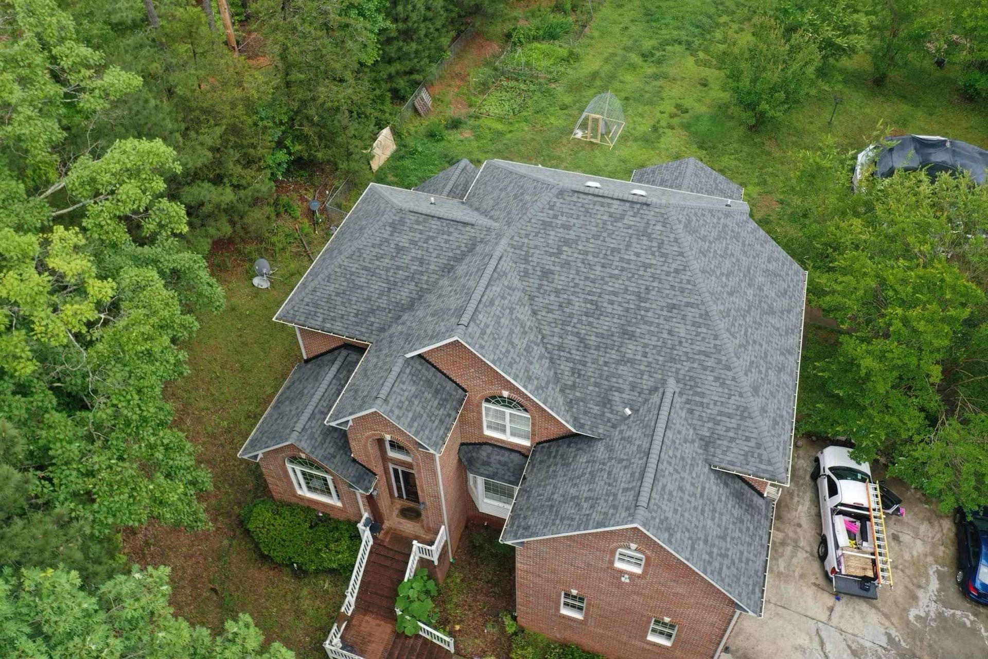 An aerial view of a large brick house with a gray roof surrounded by trees.
