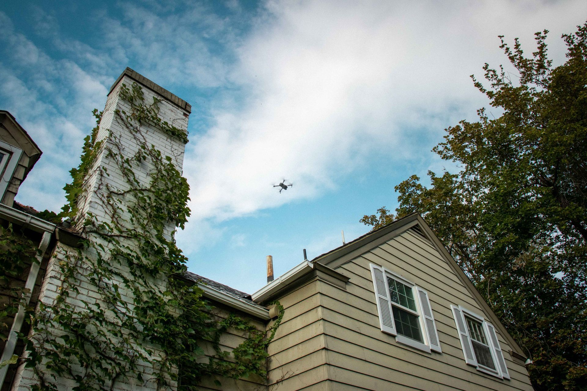 A plane is flying over a house with a chimney covered in ivy.