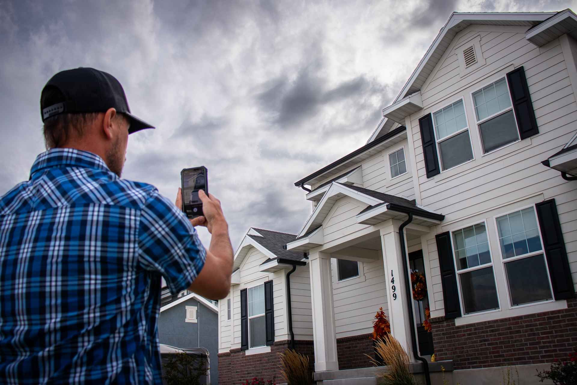 A man is taking a picture of a house with a cell phone.