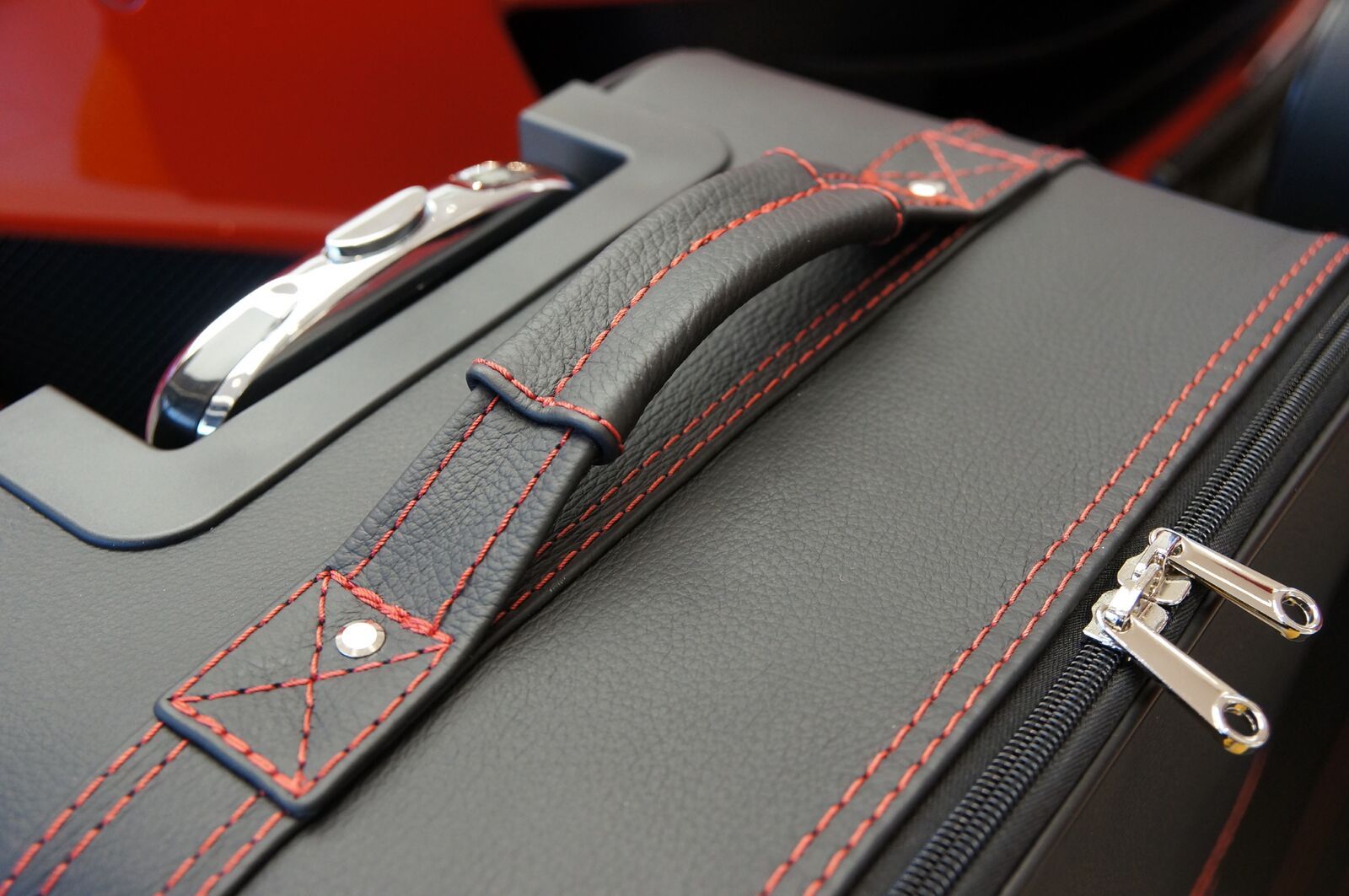 Een zwarte koffer met rode stiksels en een handvat