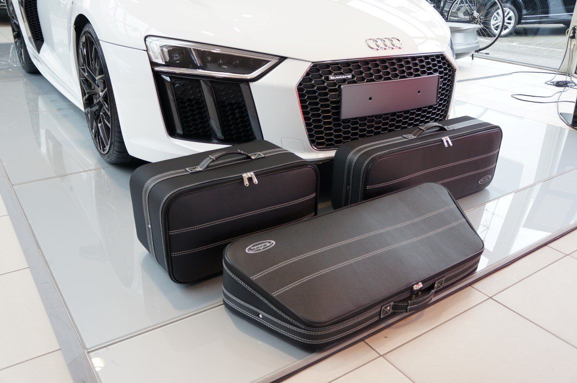 Een witte Audi R8 staat in een showroom geparkeerd met bagage ervoor.