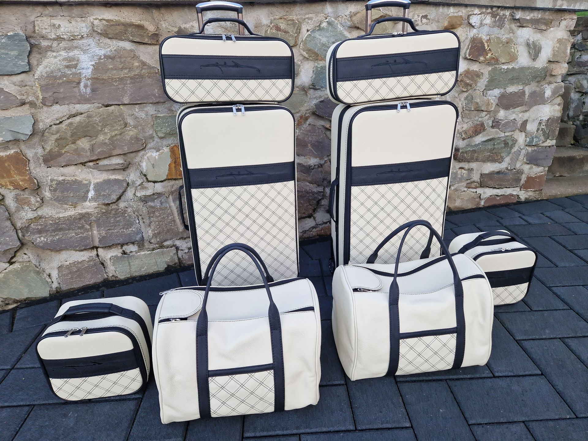 Een groep witte koffers en sporttassen staat voor een stenen muur.