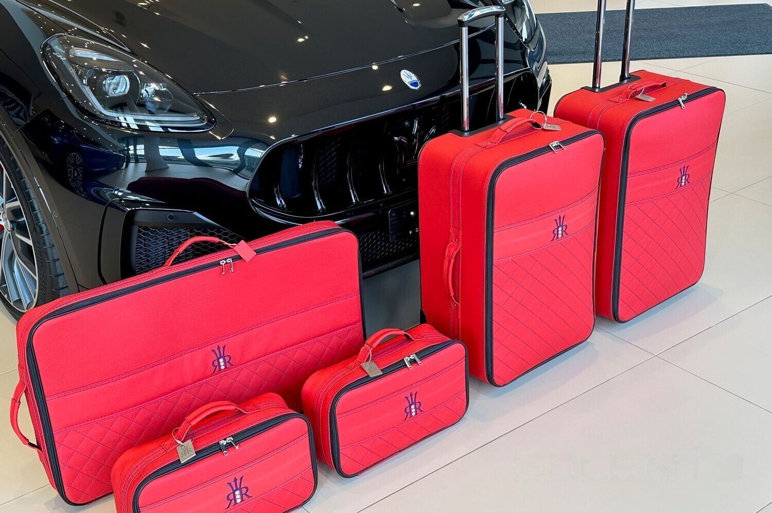 Een groep rode koffers staat voor een zwarte auto