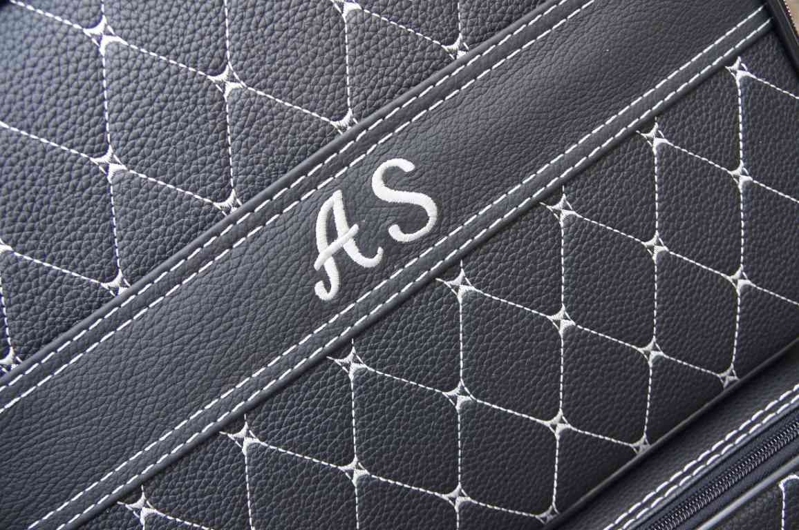 Een close-up van een zwarte leren tas met de initialen a en s erop geborduurd.