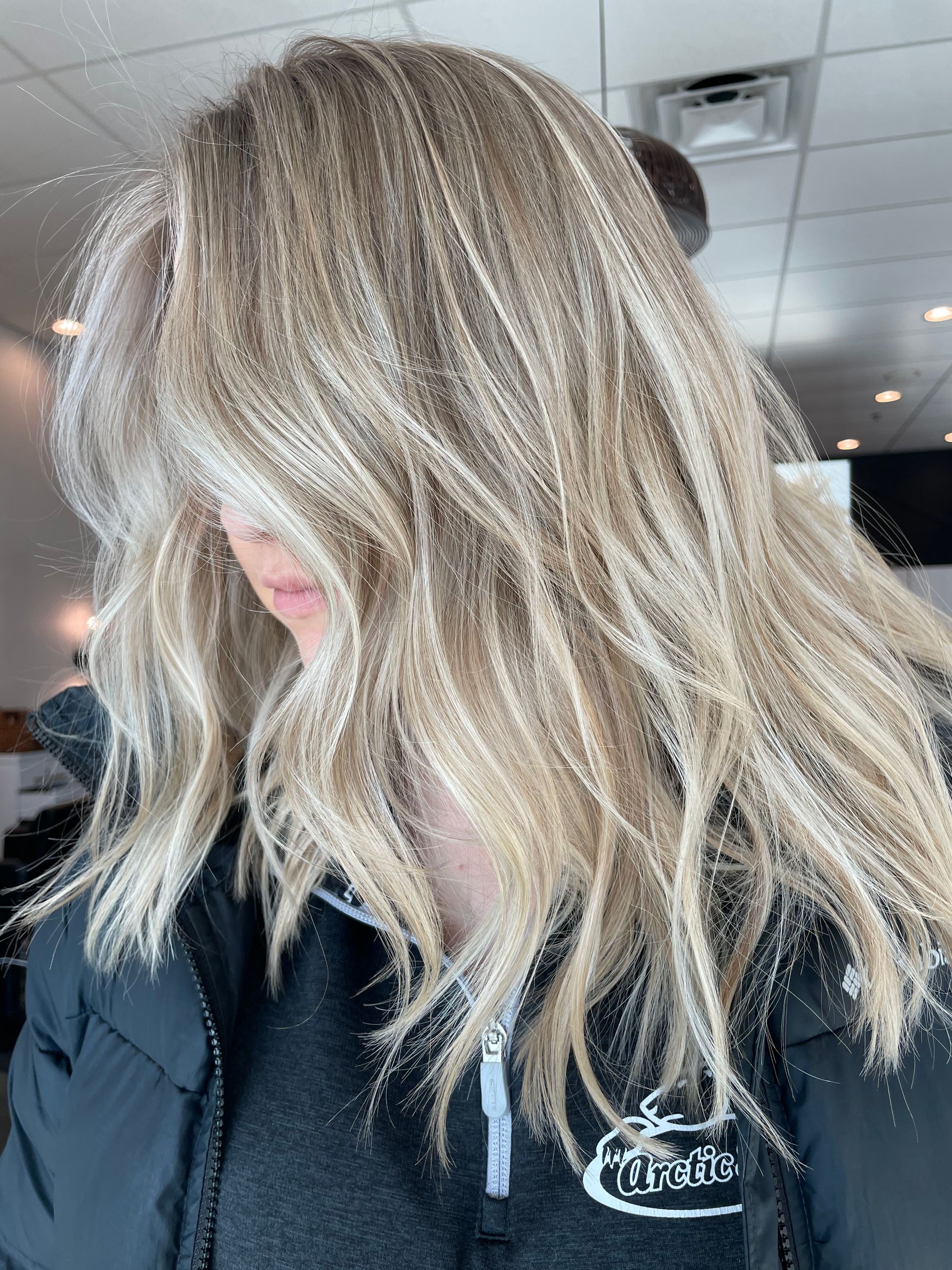 Blonde, wavy hair partially obscures a person's face; they wear a black jacket.