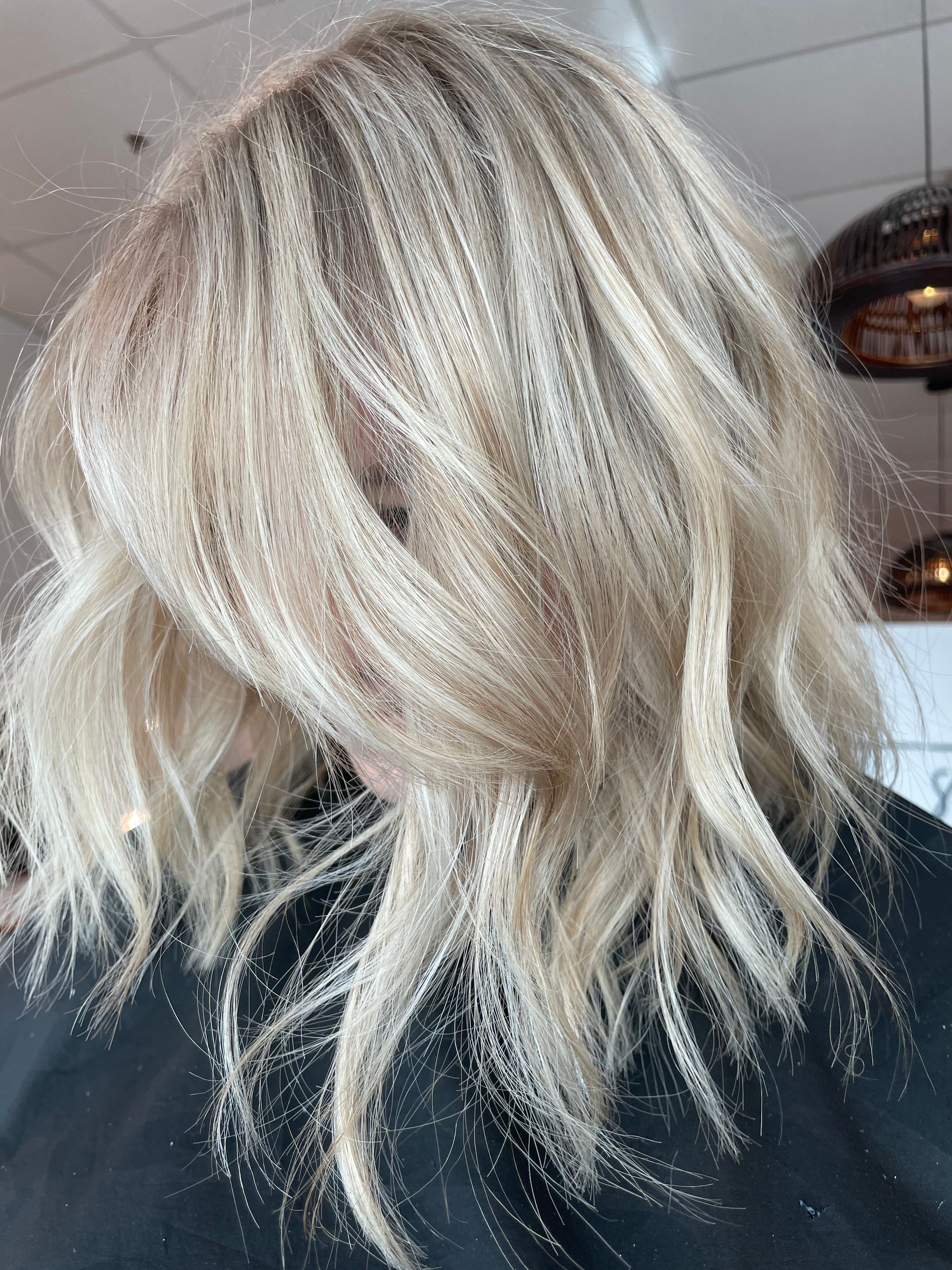 Blonde, shoulder-length hair styled with soft waves; in a salon.