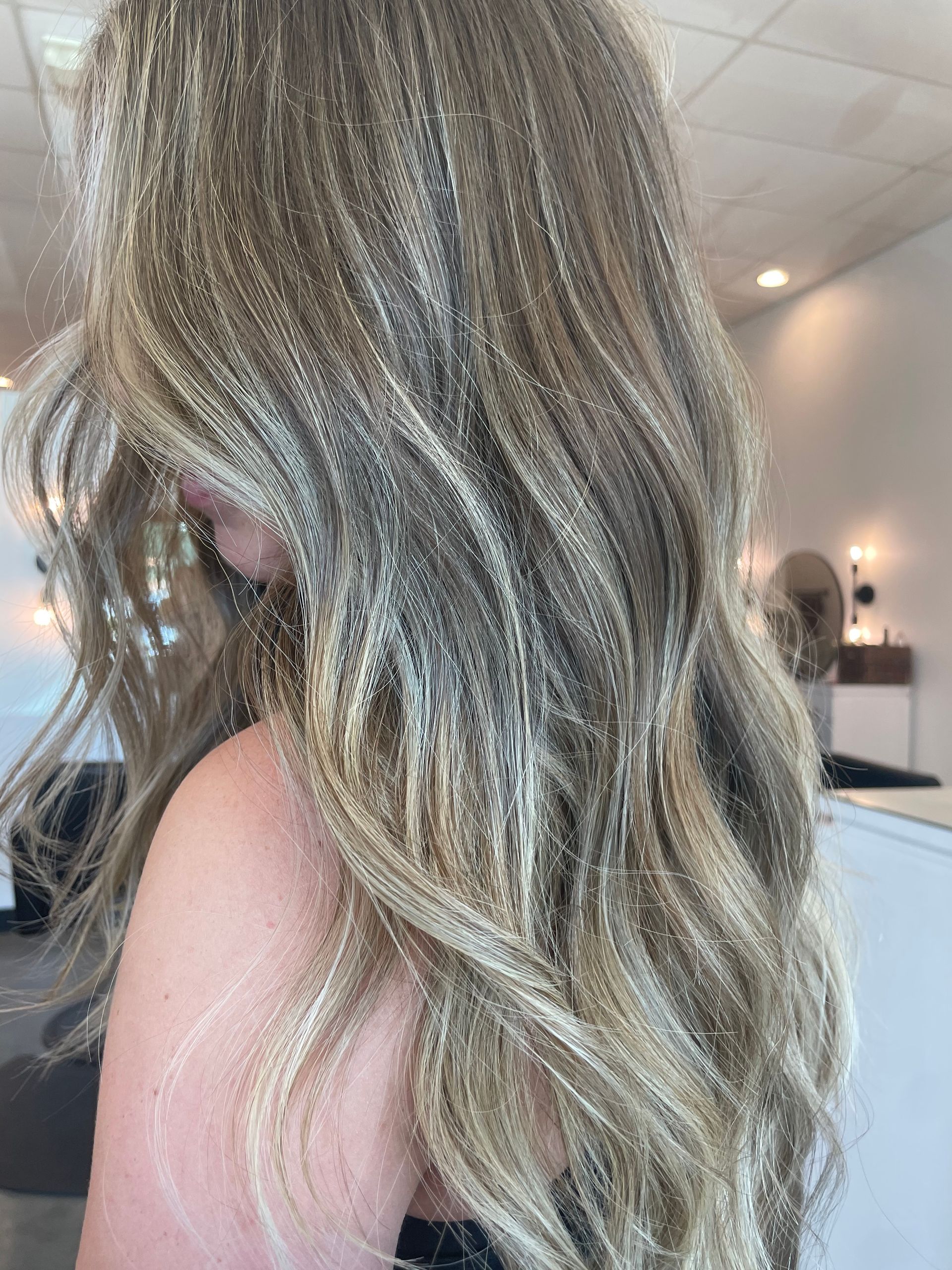 Woman with long wavy blonde hair, highlights, in a salon setting.