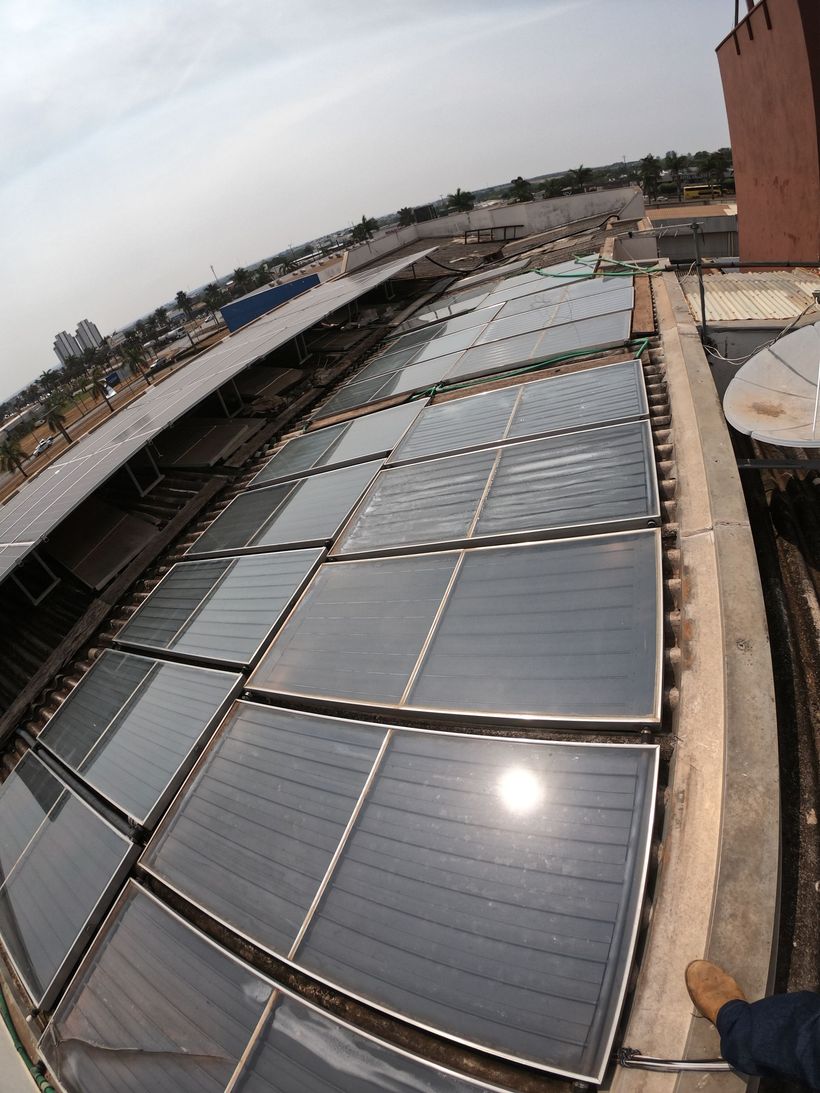 Painéis solares cobrindo um telhado sob a luz do sol, com uma paisagem urbana distante ao fundo. Lucas do rio verde
