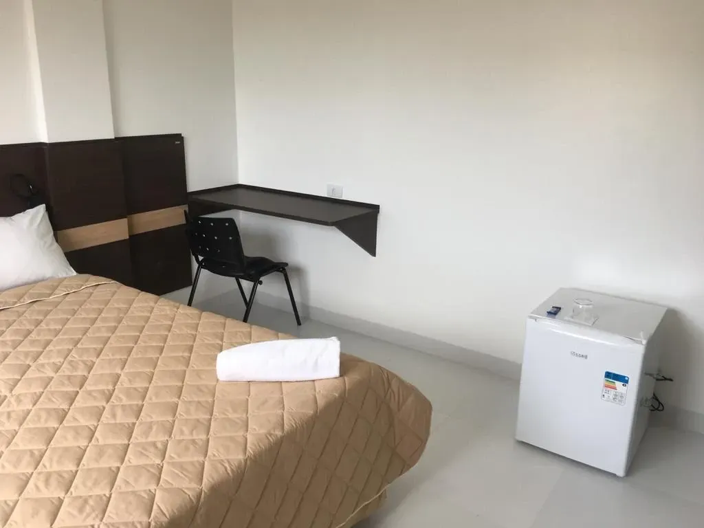 Um quarto com uma cama, escrivaninha, cadeira e uma pequena geladeira.-Executive-Hotel-MT
