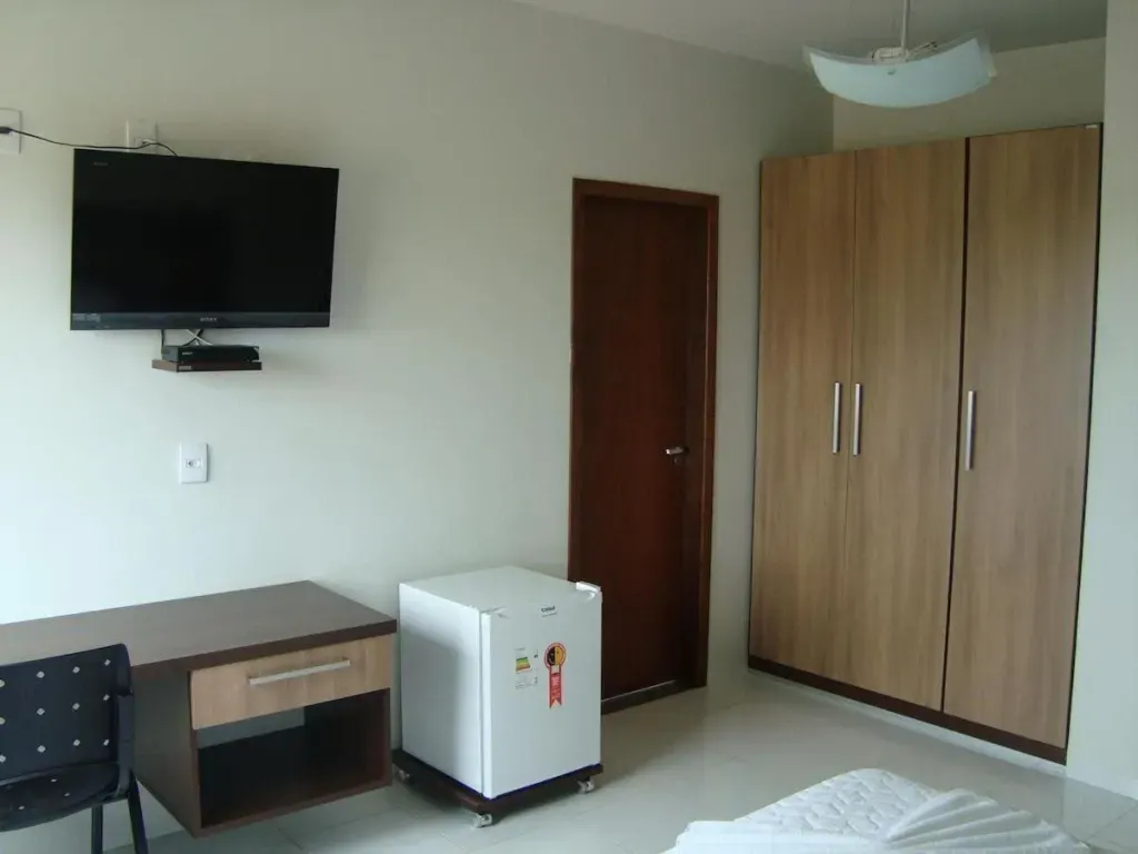 Um quarto com uma tv de tela plana e uma geladeira pequena-Executive-Hotel-MT