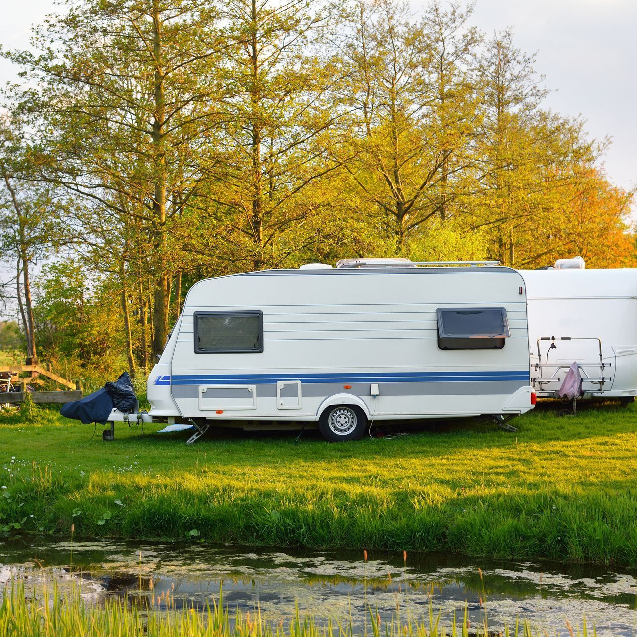 A caravan is parked in a grassy field next to a body of water.