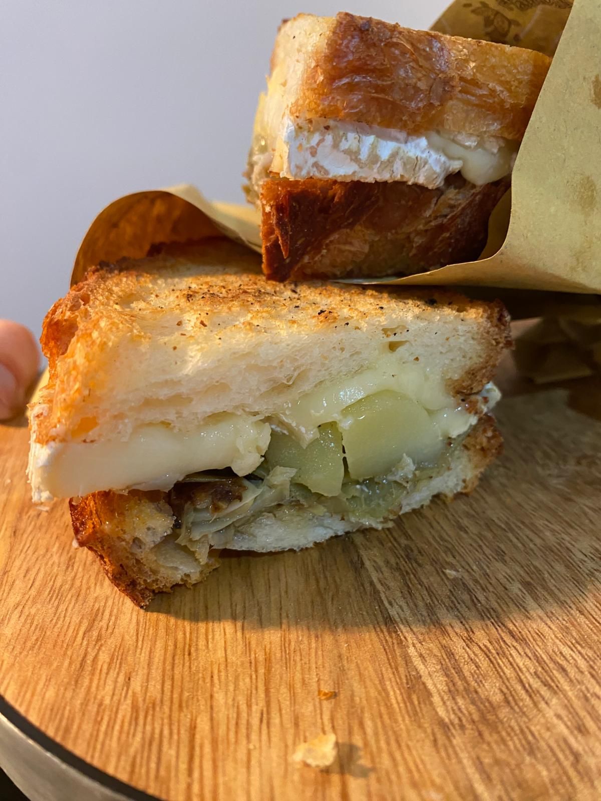Primo piano di un sandwich grigliato a fette con formaggio fuso su un tagliere di legno.