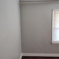 An interior corner with light gray walls, white baseboard molding, and a window with white blinds on the right wall.