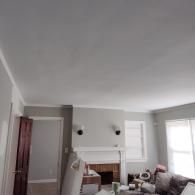 A living room with light gray walls, a white fireplace, two wall sconces, and a doorway leading to another room.
