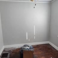 An empty room with gray walls, white trim, dark wood flooring, a ceiling fan pull chain, and a box on the floor.