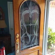 A wooden door with a large, arched window featuring decorative, etched glass patterns and a brass handle.