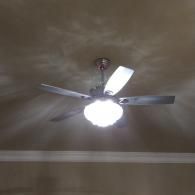 A ceiling fan with a bright, illuminated dome-style light fixture and five metallic blades.